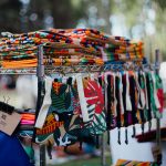 Bolsas e tecidos artesanais coloridos expostos em uma feira ao ar livre.