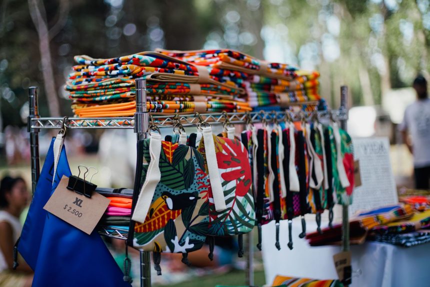 Bolsas e tecidos artesanais coloridos expostos em uma feira ao ar livre.