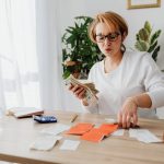 Pessoa contando dinheiro e organizando recibos sobre uma mesa, com uma calculadora ao lado.