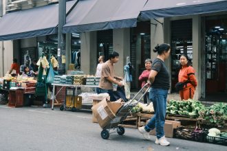 Consumidores circulam por uma feira livre em São Paulo entre barracas de hortaliças e outros produtos.