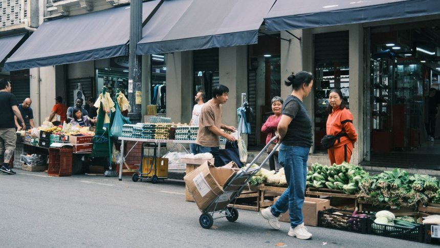 Consumidores circulam por uma feira livre em São Paulo entre barracas de hortaliças e outros produtos.