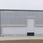 Fachada de um grande galpão logístico moderno, com portas fechadas para carga e descarga.