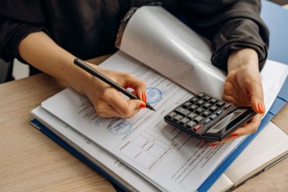 Profissional de contabilidade usa uma calculadora e assina documentos financeiros em uma mesa de trabalho.