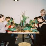 Mulheres participam de uma oficina de artesanato natalino e confeccionam guirlandas em ambiente interno.