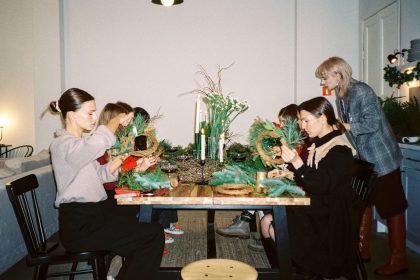 Mulheres participam de uma oficina de artesanato natalino e confeccionam guirlandas em ambiente interno.