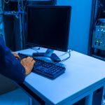 Profissional de tecnologia opera um computador em uma sala de servidores, gerenciando sistemas de rede e dispositivos conectados.